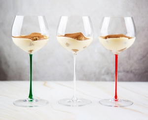 A RIEDEL Fatto A Mano Oaked Chardonnay glass in green filled with white wine on a white background. 