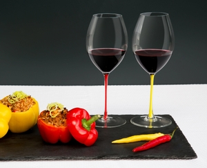 A RIEDEL Fatto A Mano Syrah glass in red filled with red wine on a white background. 