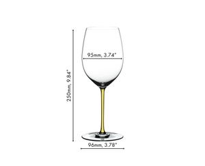 A RIEDEL Fatto A Mano Cabernet/Merlot glass in yellow filled with red wine on a white background. 