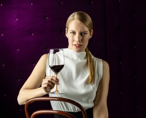 A RIEDEL Fatto A Mano Cabernet/Merlot glass in orange filled with red wine on a white background. 