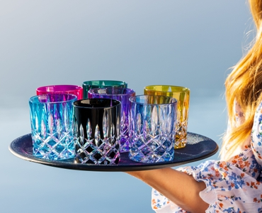 A woman holds a tray of glasses with the different colors from the RIEDEL Laudon collection including the RIEDEL Laudon Amber glass. 