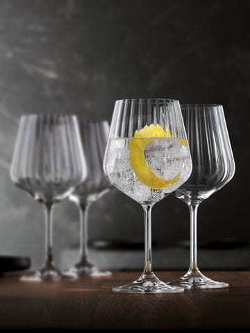 Two stemmed NACHTMANN Masterpiece glasses, one is filled with a Gin and Tonic and a lemon zest, the other one behind is empty. In the background are two more empty Masterpiece glasses.<br/>