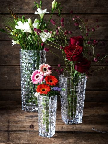 Drei Kristallvasen NACHTMANN Bossa Nova in verschiedenen Größen, jede von ihnen gefüllt mit einem anderen Blumenstrauß, auf einer hölzernen Anrichte.<br/>