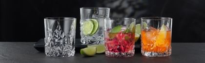 Four NACHTMANN Sculpture Whiskey tumblers on a table, three of them filled with different alcoholic and non-alcoholic drinks. Inbetween the glasses the table is decorated with slices of lime.<br/>