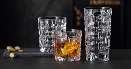 The NACHTMANN Bossa Nova SOF filled with whisky next to the empty Bossa Nova longdrink glass on a black stone sideboard. Behind them the empty Bossa Nova tumbler.