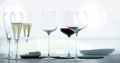 Die SPIEGELAU Willsberger Anniversary Serie auf der Anrichte. Zwei von drei Champagnergläsern sind mit Champagner gefüllt, daneben ein Schälchen mit Meersalz, gefolgt von einem leeren Weißweinglas, gefüllten Bordeauxglas und einem leeren Burgunderglas.<br/>