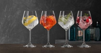 Vier SPIEGELAU Gin und Tonic Gläser auf einem Holztisch, jedes davon gefüllt mit einem anderen Gin-Cocktail.<br/>
