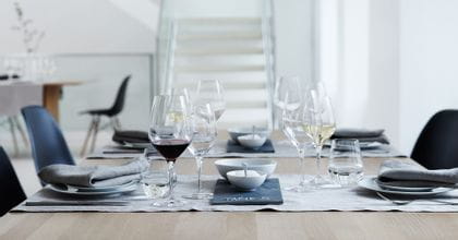 A laid table with three SPIEGELAU glasses at each of the places. On the left place, a with red wine filled Authentis Burgundy glass, an empty white wine glass and a with water filled Authentis Casual tumbler. On the right the Bordeaux glass is empty but the white wine glass is filled.<br/>
