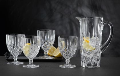 The NACHTMANN Noblesse pitcher filled with water, ice cubes and lemon slices besides four NACHTMANN Noblesse goblets of which one is filled with water, ice and a lemon slice.<br/>