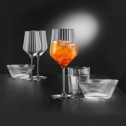 Gefülltes NACHTMANN Aperitivo Spritz Glas neben Trinkglas und Schale. Im Hintergrund weitere Gläser und eine Schale.