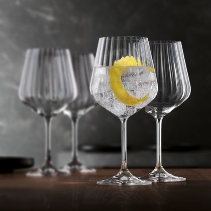 Two stemmed NACHTMANN Masterpiece glasses, one is filled with a Gin and Tonic and a lemon zest, the other one behind is empty. In the background are two more empty Masterpiece glasses.<br/>