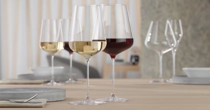 <br/>A SPIEGELAU Definition Bordeaux glass filled with red wine and a SPIEGELAU Definition white wine glass filled with white wine on a table. In the background are the same filled wine glasses again.<br/>