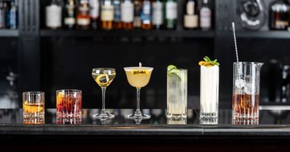 drink specific glasses stand in a row on a bar, bottles in the background