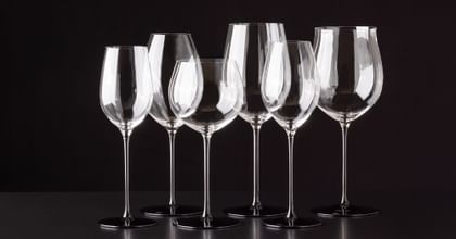 various RIEDEL wine glasses lined up against black background