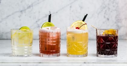 Nachtmann Highland Tumblers in a line on a white bench filled with colourful cocktails.