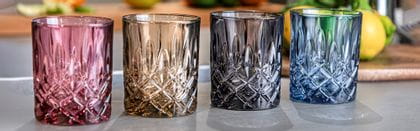 Four NACHTMANN Noblesse Whisky Tumblers in Berry, Taupe, Smoke and Vintage Blue on a benchtop.
