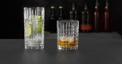 Das NACHTMANN Highland Square Longdrinkglas gefüllt mit einem klaren Drink mit Limette und Eiswürfeln und der Tumbler gefüllt mit Whiskey auf Eis.<br/>