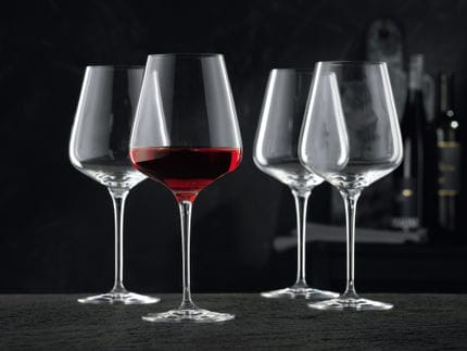 Four NACHTMANN Vinova Bordeaux glasses, one of them filled with red wine.<br/>