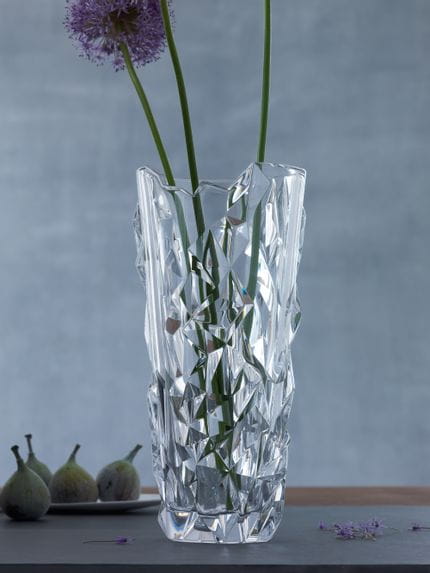 Le vase NACHTMANN Sculpture avec trois fleurs d'allium sur de longues tiges. En arrière-plan, une assiette avec quatre figues.<br/>