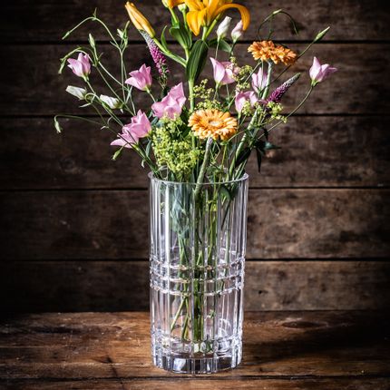 The crystal NACHTMANN vase Square, filled with orange and pink flowers, on a dark wooden sideboard.<br/>