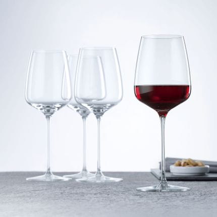 Four SPIEGELAU Willsberger Anniversary Red Wine glasses, one of them filled with red wine.<br/>