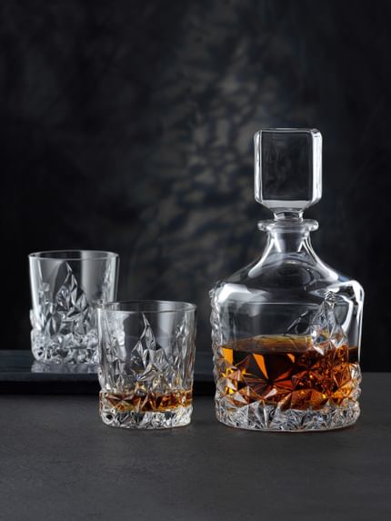 Die NACHTMANN Sculpture Whiskey-Karaffe neben dem NACHTMANN Sculpture Whiskey-Glas, beide gefüllt mit Whiskey. Im Hintergrund ein leerer Sculpture Becher auf einem Serviertablett.<br/>