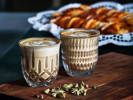 NACHTMANN Barista Ethno- und Noblesse-Cappuccino-/Flat White-Glas, mit Kaffee gefüllt, im Hintergrund Gebäck