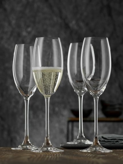 Vier NACHTMANN Vivendi Champagnerflöten auf einem Holztisch, eine davon mit Champagner gefüllt.<br/>