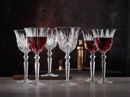 Six Nachtmann Palais Red Wine Goblets scattered on a marble bench. Three filled with wine and three without wine.