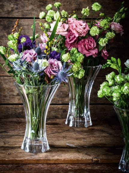 I vasi di cristallo NACHTMANN Saphir, riempiti con bouquet di fiori colorati nei colori rosso, verde, viola e blu, su una credenza di legno.<br/>