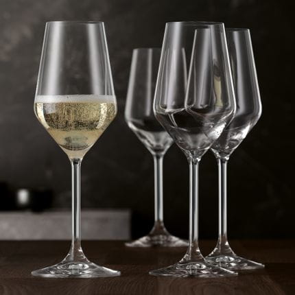 Four SPIEGELAU Style Champagne glasses on a wooden table. One glass is filled with sparkling wine.<br/>