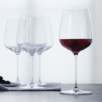 Four SPIEGELAU Willsberger Anniversary Bordeaux glasses, one of them filled with red wine.<br/>