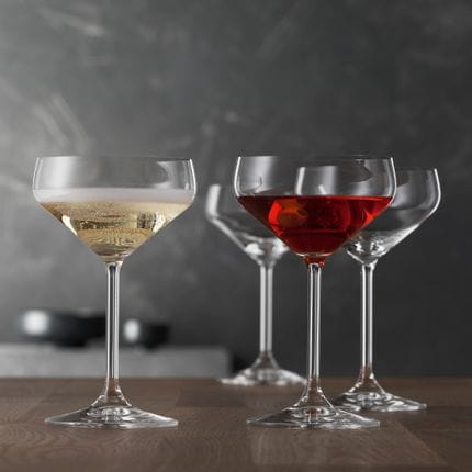 Quattro bicchieri Coupette in stile SPIEGELAU. Un bicchiere in primo piano è riempito di Champagne, un altro di una bevanda rossa.<br/>