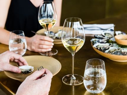 Two RIEDEL Veritas Champagne glasses on a table setting filled with champagne next to oysters.
