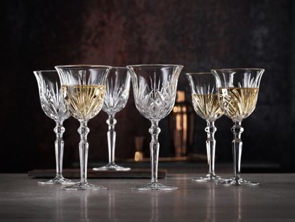 Six Nachtmann Palais White Wine Goblets scattered on a marble bench. Three filled with wine and three without wine.