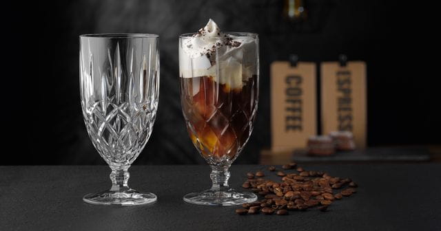 The NACHTMANN Noblesse iced beverage glass filled with an iced coffee with cream on it. On the left the same glass but empty. On the right, as a decoration, are coffee beans.<br/>