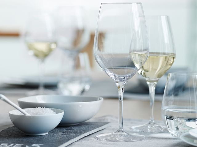 Una copa SPIEGELAU Authentis Bordeaux sobre una mesa puesta. Detrás, una copa de vino blanco llena de la línea Authentis y un vaso SPIEGELAU Authentis Casual lleno de agua se muestran a la derecha.<br/>