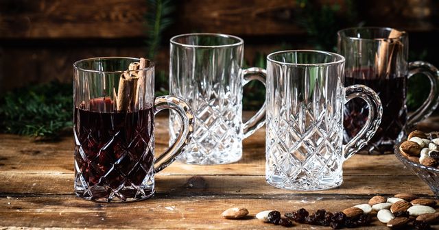 The NACHTMANN Noblesse tea glass with mulled wine and cinnamon sticks in it on a wooden sideboard. Next to it are two empty and one filled Noblesse tea glasses, almonds, raisins and pine branches.<br/>