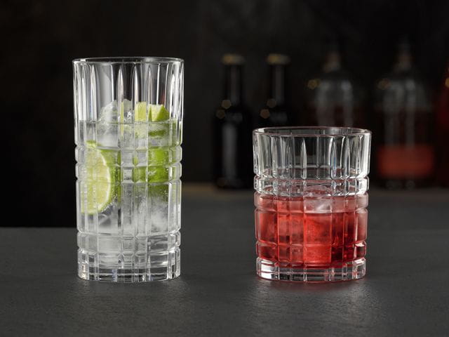 Das NACHTMANN Highland Square Longdrinkglas gefüllt mit einem klaren Drink mit Limette und Eiswürfeln und der Tumbler gefüllt mit einem Campari Drink auf Eis.<br/>