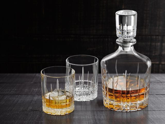 El decantador de la colección SPIEGELAU Perfect Serve, lleno de whisky, junto a dos vasos Perfect, uno lleno de whisky con hielo.<br/>